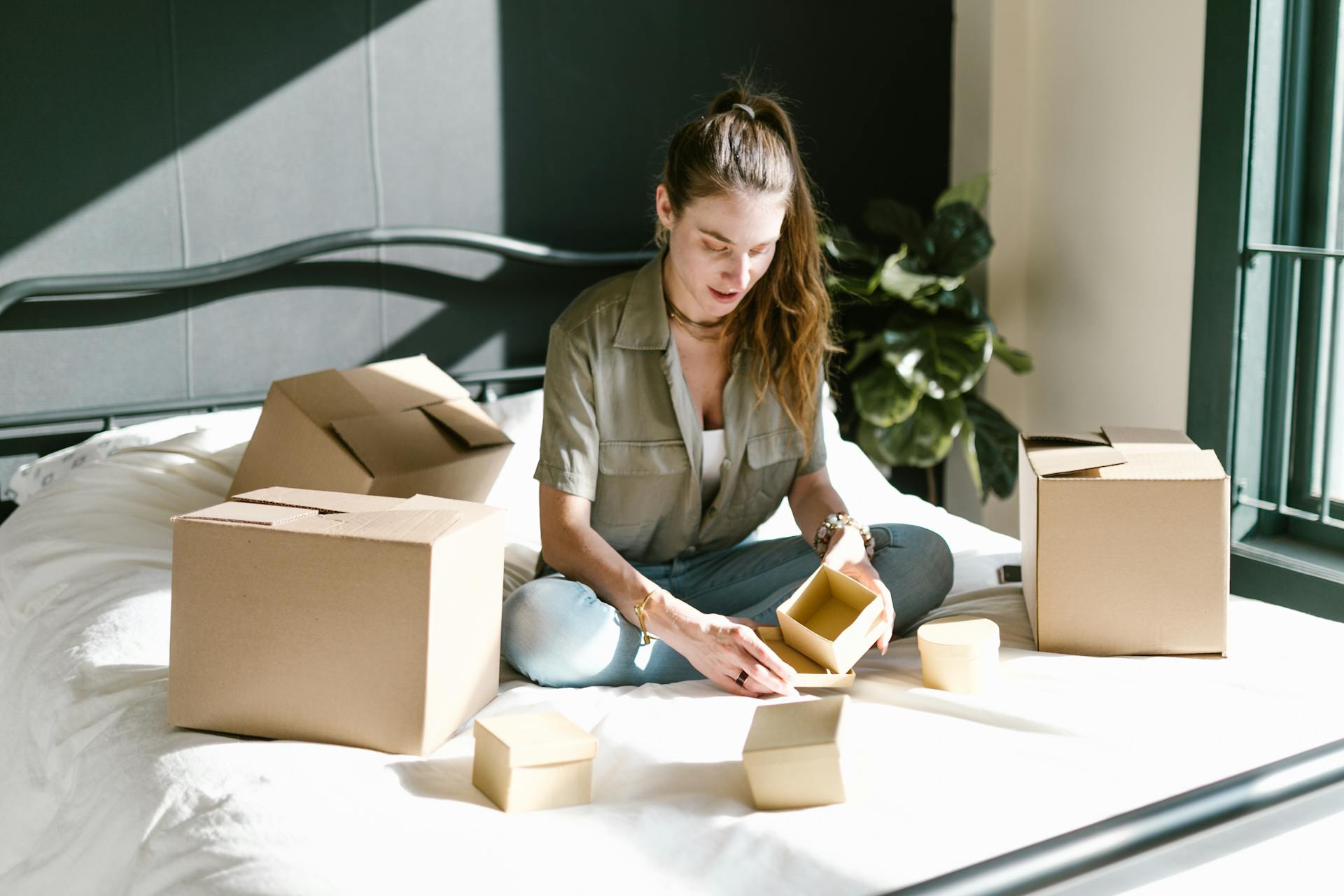 Young woman packing cardboard boxes in a sunlit room, embodying small business or moving themes.