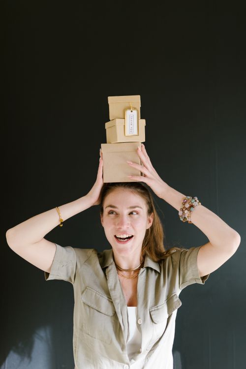 Free A cheerful young woman balances gift boxes on her head against a black background. Stock Photo