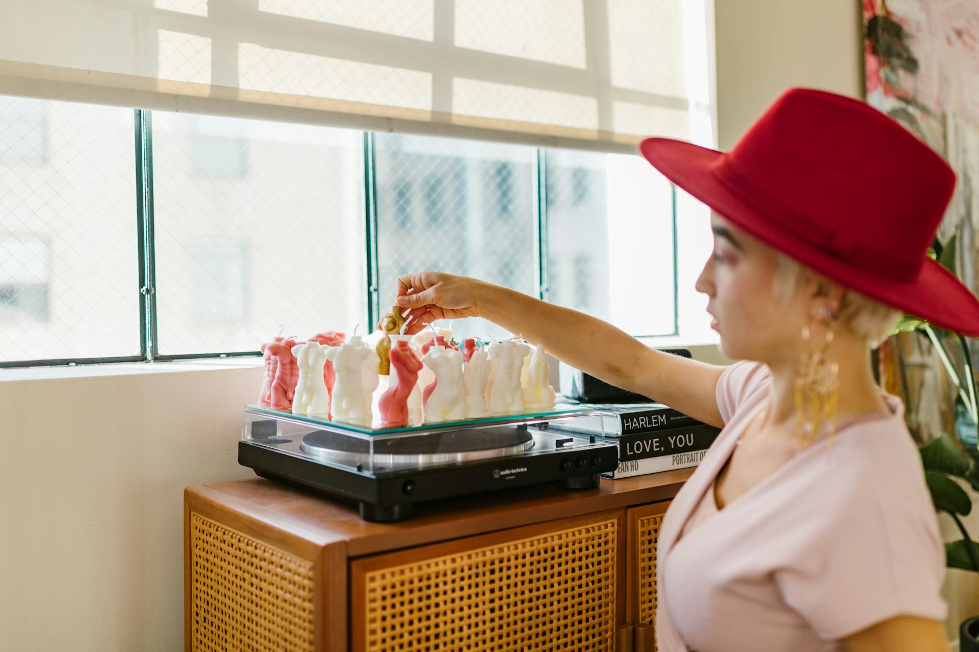 A woman in a red hat arranges candles on a record player, creating a cozy and artistic interior vibe.