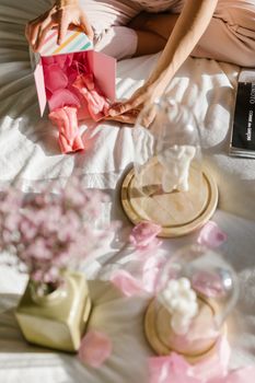 Colorful gift packaging with pink flowers and candles under glass domes on a cozy bed.