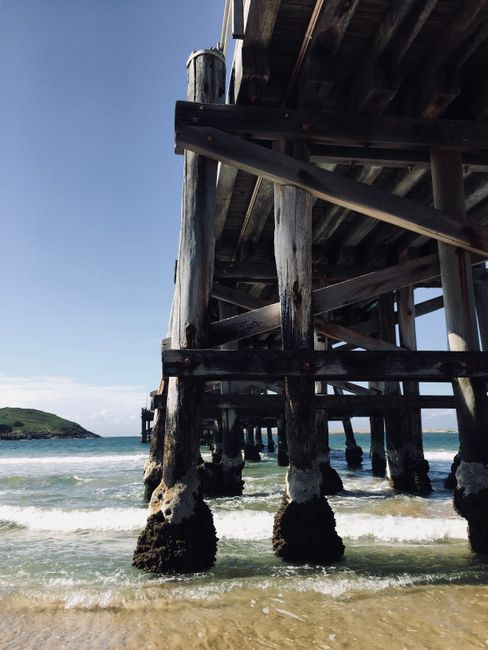 Perspective view of a wooden pier over ocean waves, capturing a sunny coastal scene.