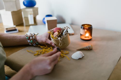 Person Holding a Box of Colored Shells with Scented Candle on a Table