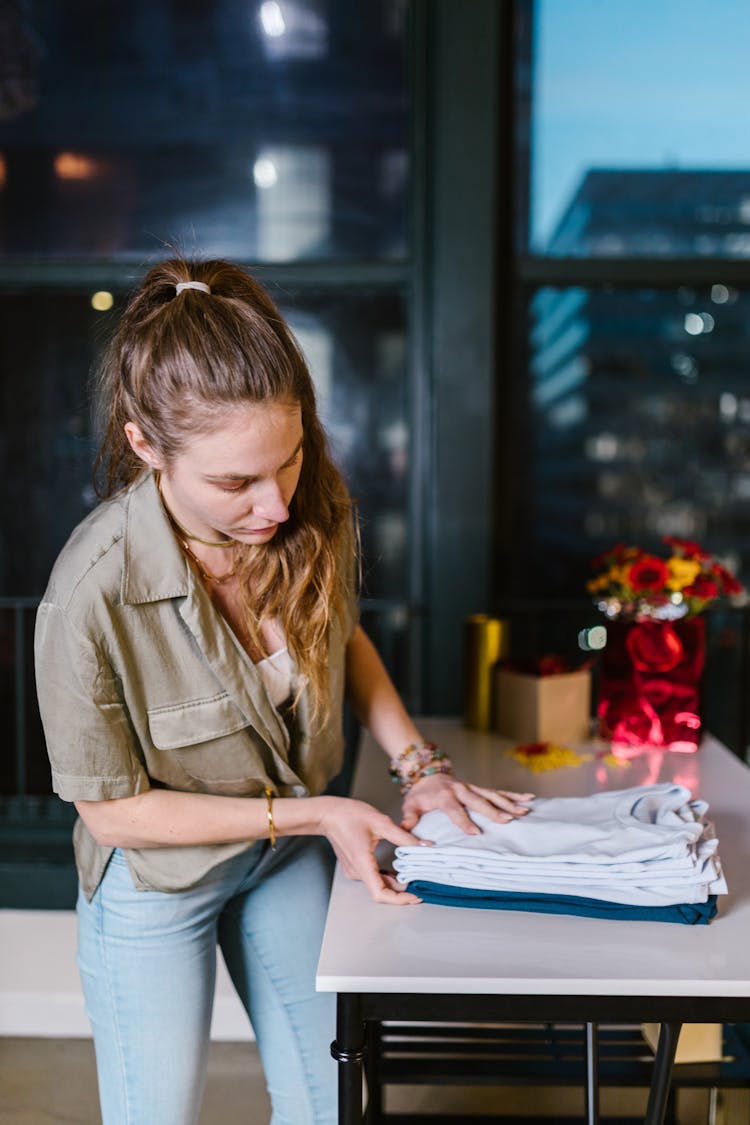 Woman Folding Clothes On White Table