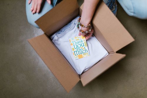 Free A person packing a white t-shirt with a thank you card into a cardboard box. Stock Photo