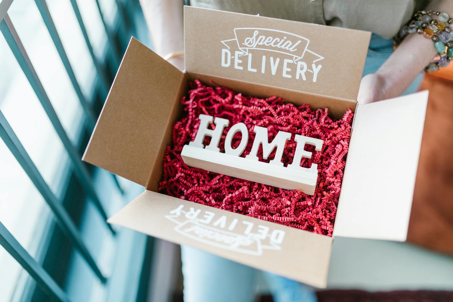 Box opened to reveal HOME decoration amidst red packing material, labeled Special Delivery.