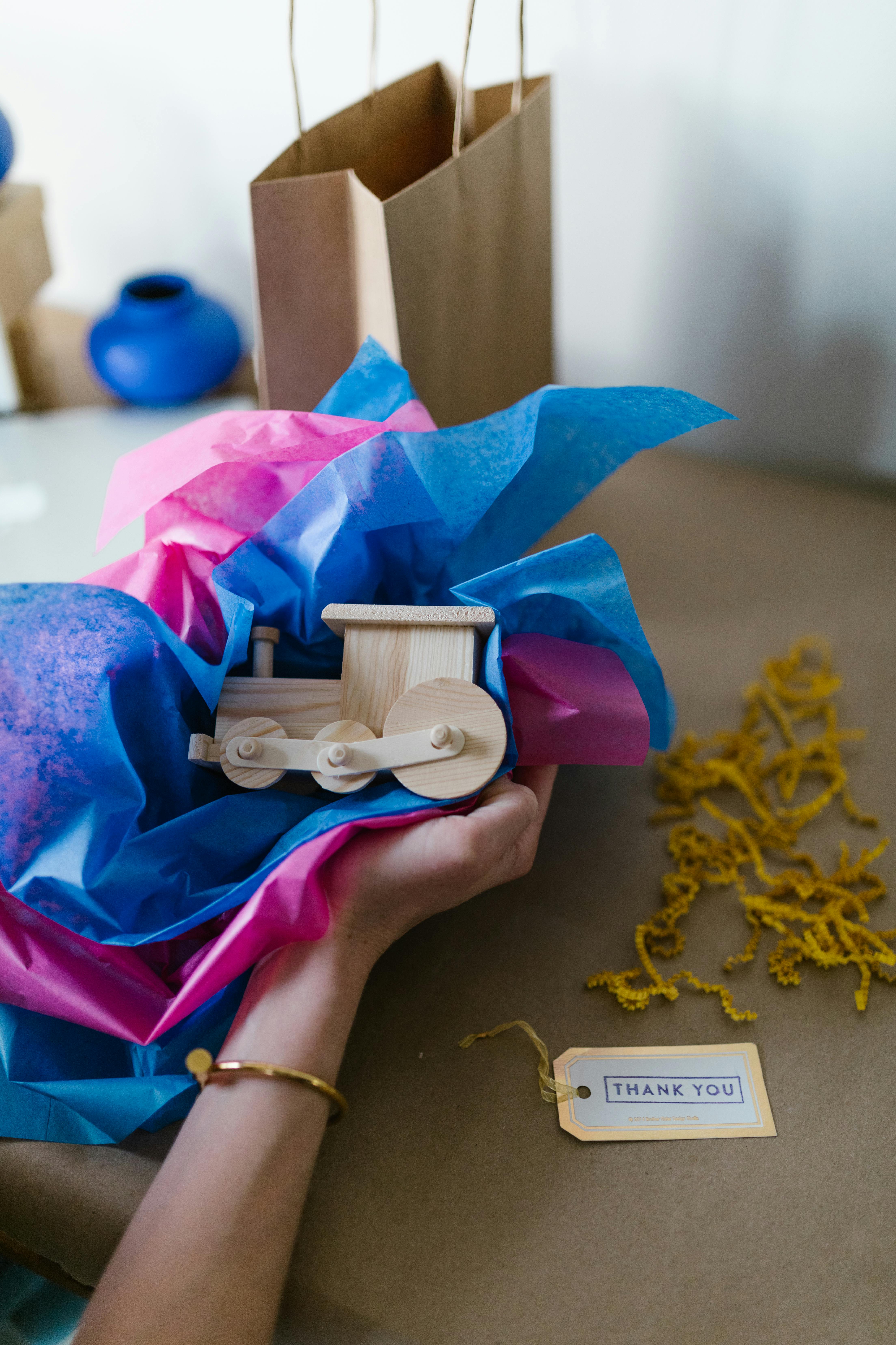 Hands wrapping a wooden toy train with colorful tissue paper, ideal for gift presentation.