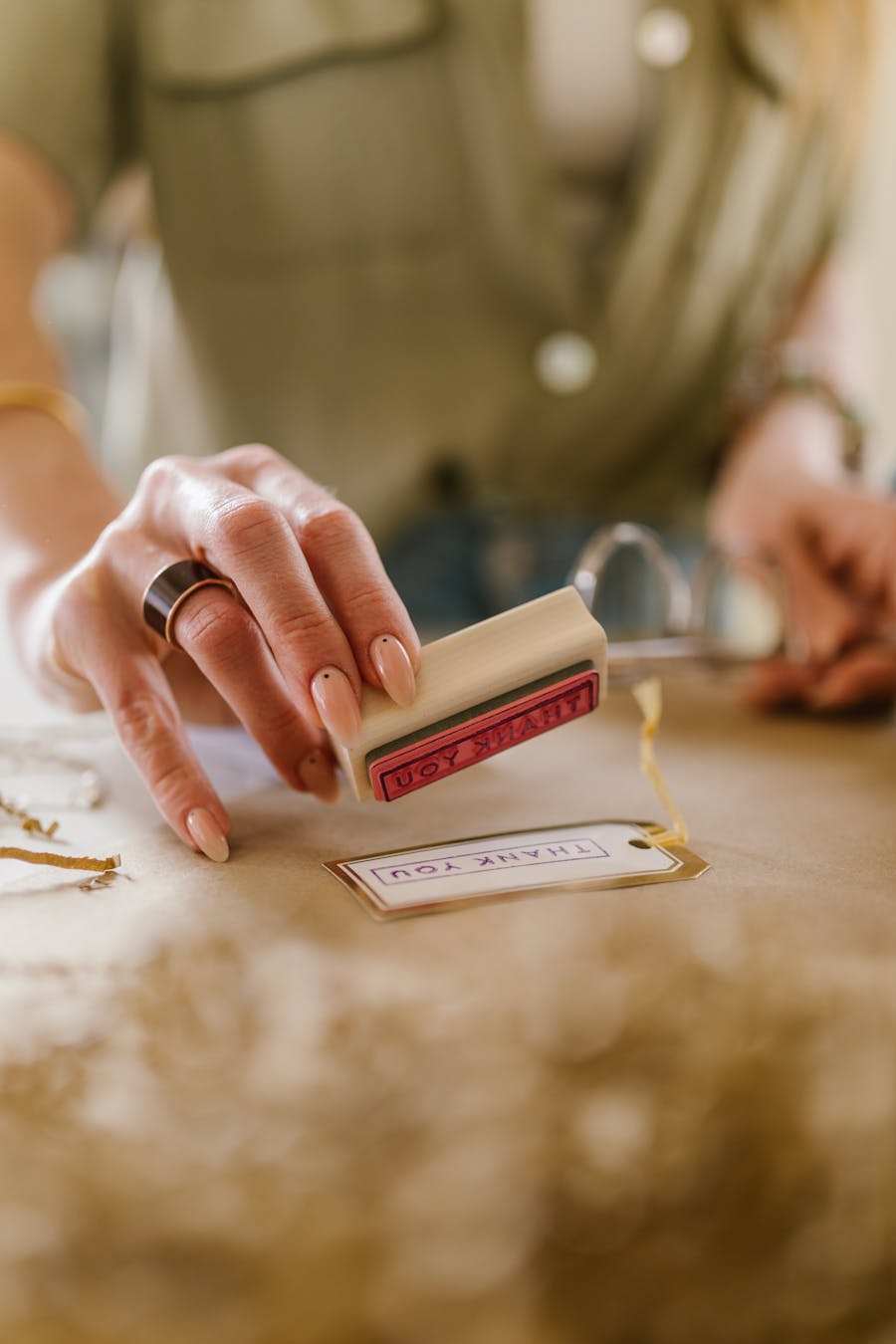 Close-up of a woman's hand stamping a thank you card on a craft table.