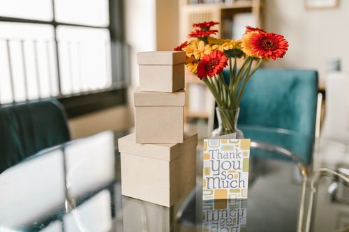Free A stylish thank you card with flowers and cardboard boxes on a modern glass table, perfect for gratitude themed designs. Stock Photo