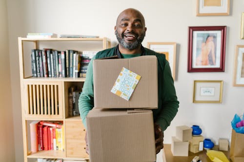 Close-Up Shot of a Man Holding Cardboard Boxes while Smiling 