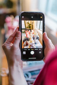 Hands holding smartphone to photograph artistic sculpture display indoors.