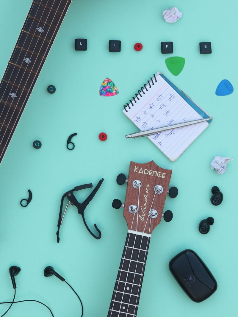 A ukulele with a notepad and picks on a teal background