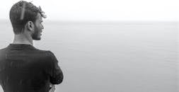 一个男人站在海边，凝视着雾蒙蒙的地平线，身影映照出孤独与宁静