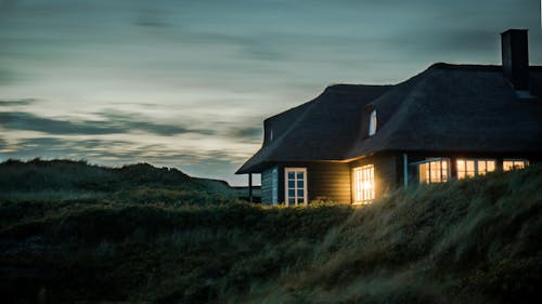 серый дом с камином в окружении травы под бело серым облачным небом