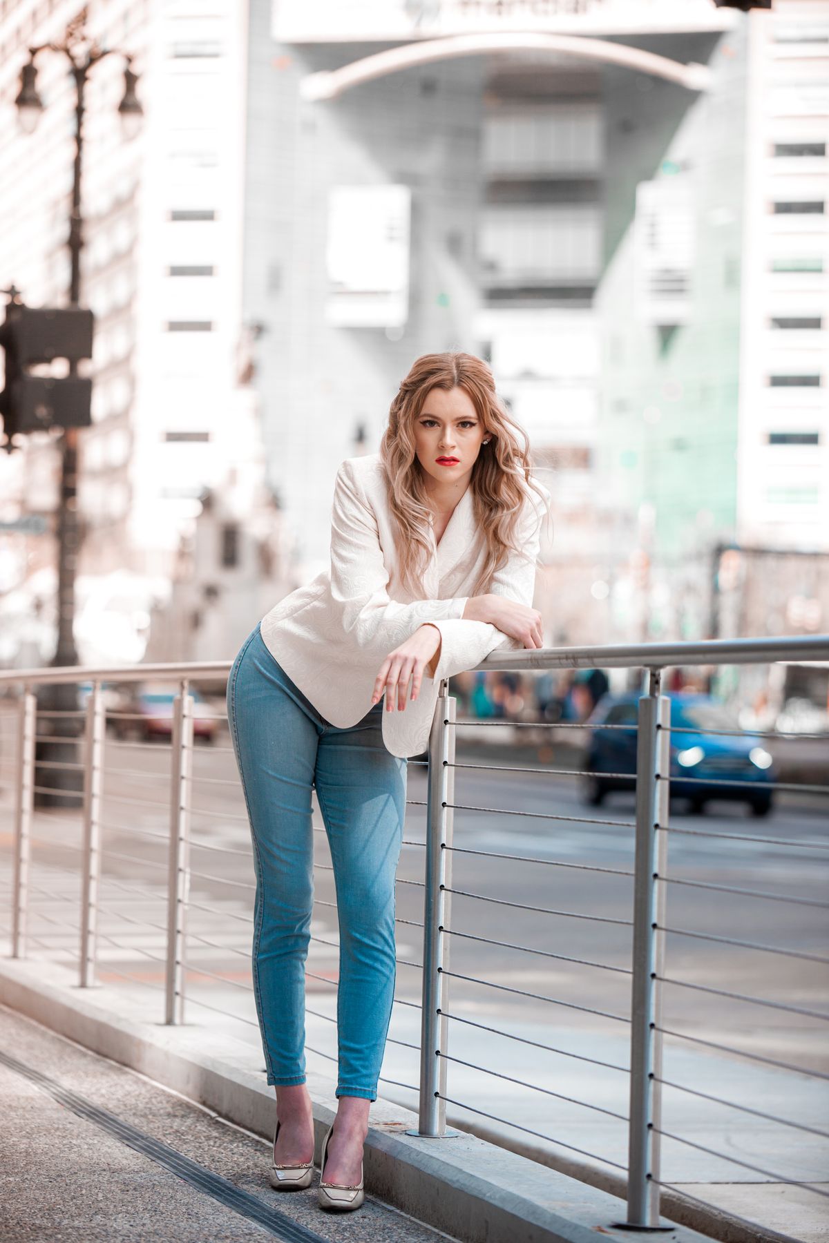 Woman in a white blazer posing beside a city railing