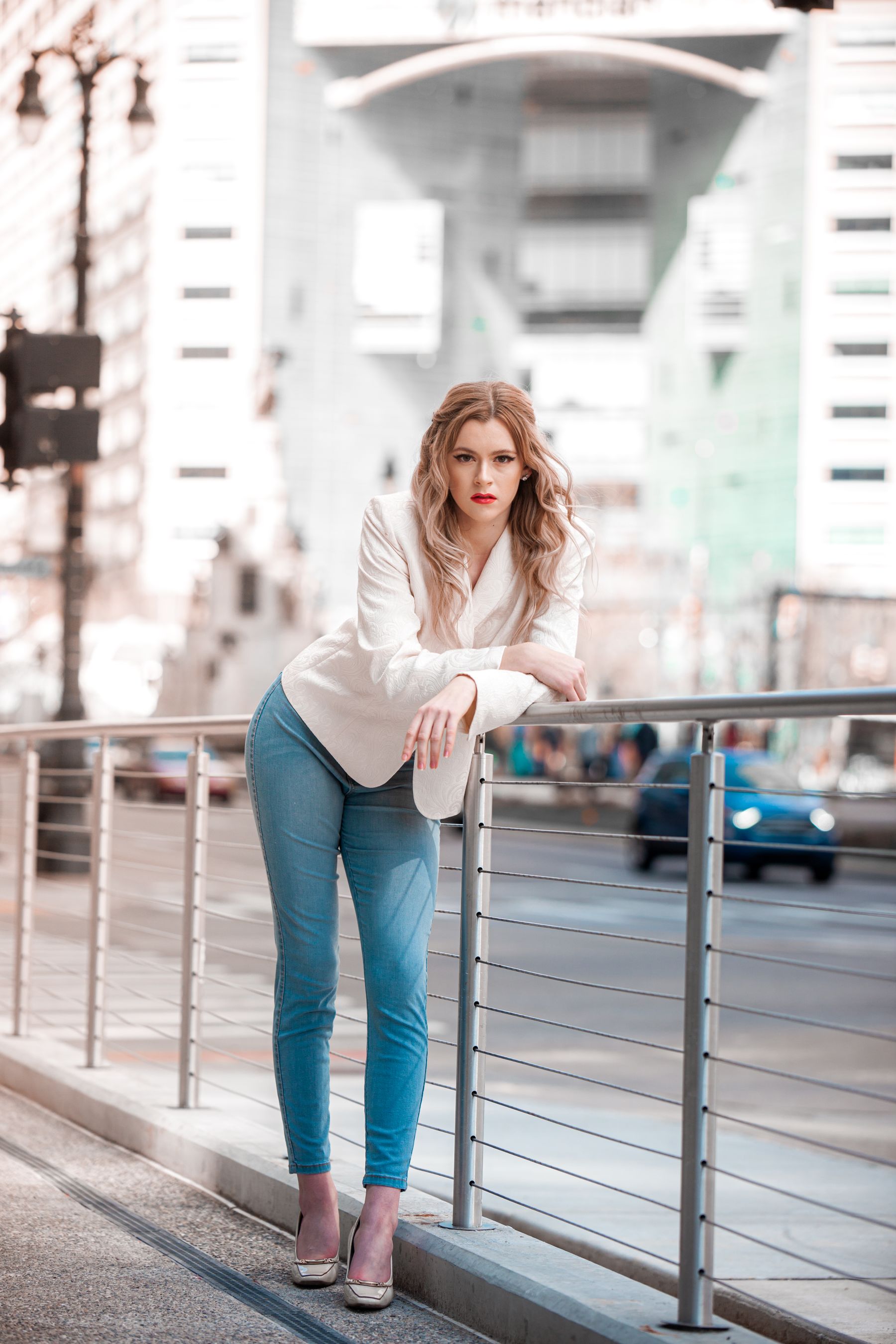 Stylish woman in a white blazer posing beside a city railing