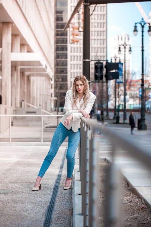 Woman in White Blazer and Blue Jeans Leaning on Metal Railing