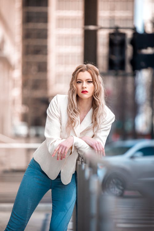 A Woman in White Blazer and Blue Jeans Standing on the Street