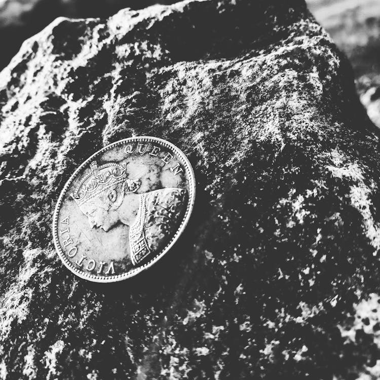 Vintage silver coin featuring Queen Victoria, resting on a textured rock in monochrome