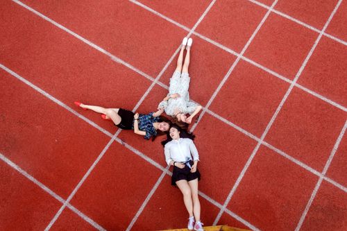 Free Three young women lying on a red running track, viewed from above, showcasing a relaxed and carefree lifestyle. Stock Photo