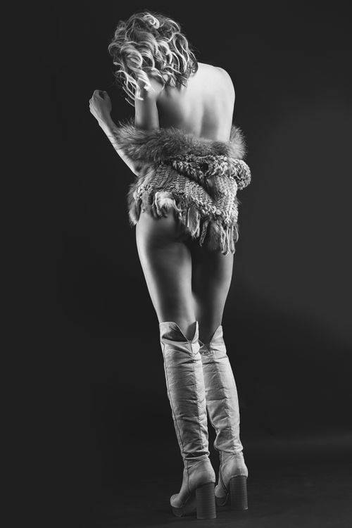 Free Black and white artistic portrait of a woman with faux fur and boots, showcasing elegance and sensuality. Stock Photo