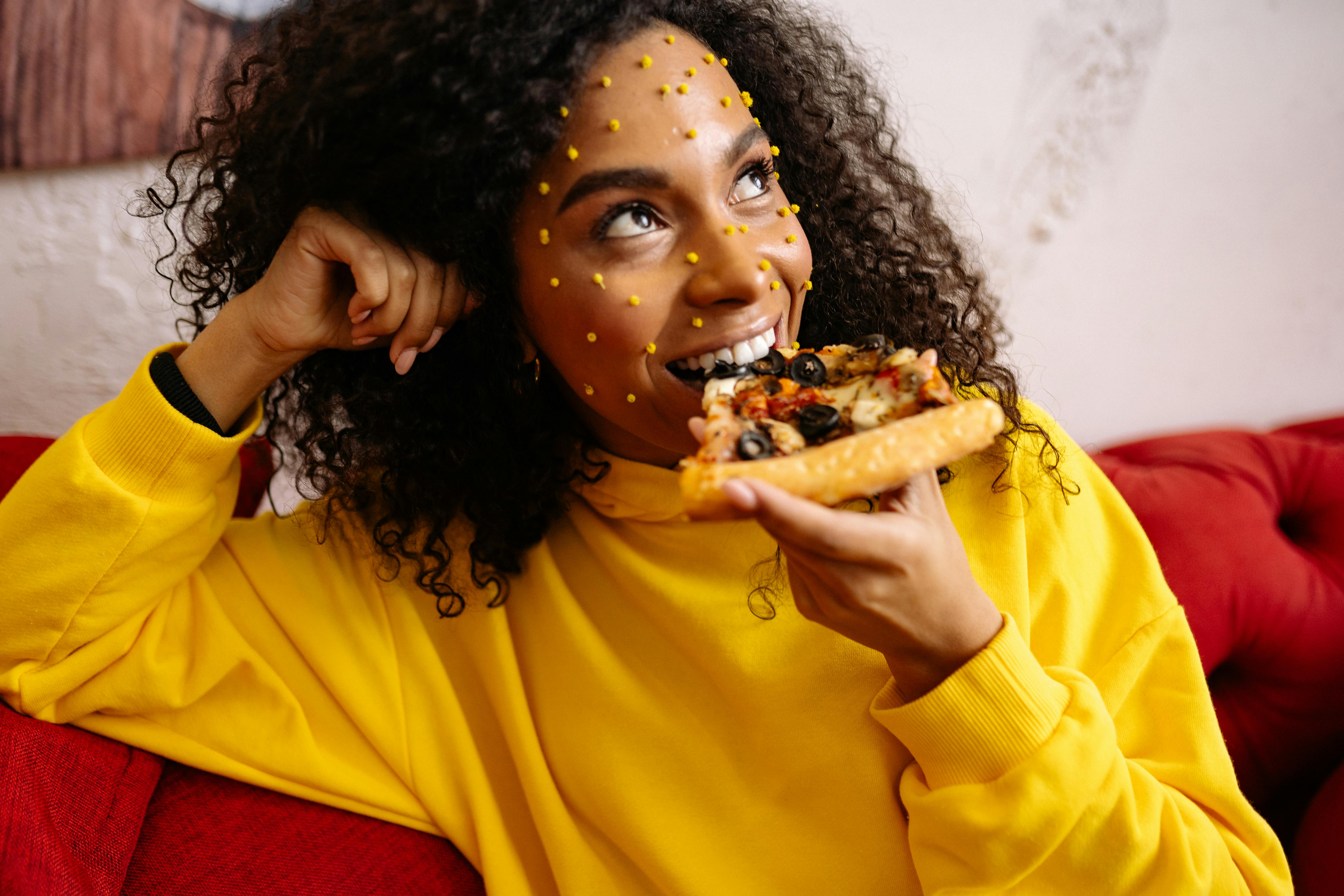 Foto profissional gratuita de cabelo cacheado, comendo pizza, fechar se,  jaqueta amarela, maquiagem criativa, olhando para longe