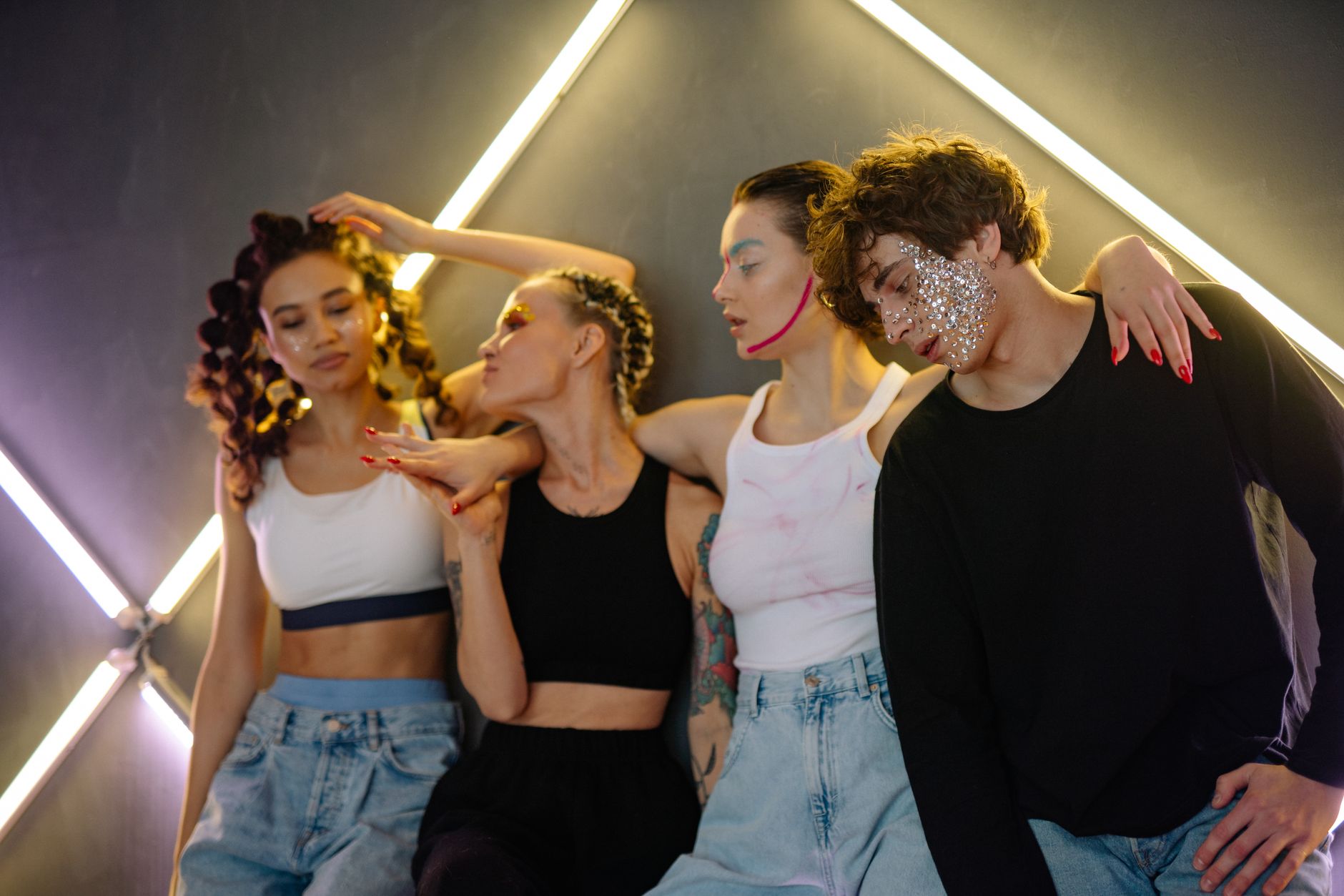 A vibrant group of young adults with artistic makeup posing indoors, showcasing creative fashion and glitter.