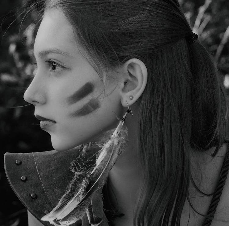 A Woman Wearing Feather Earrings And Marks On Cheeks