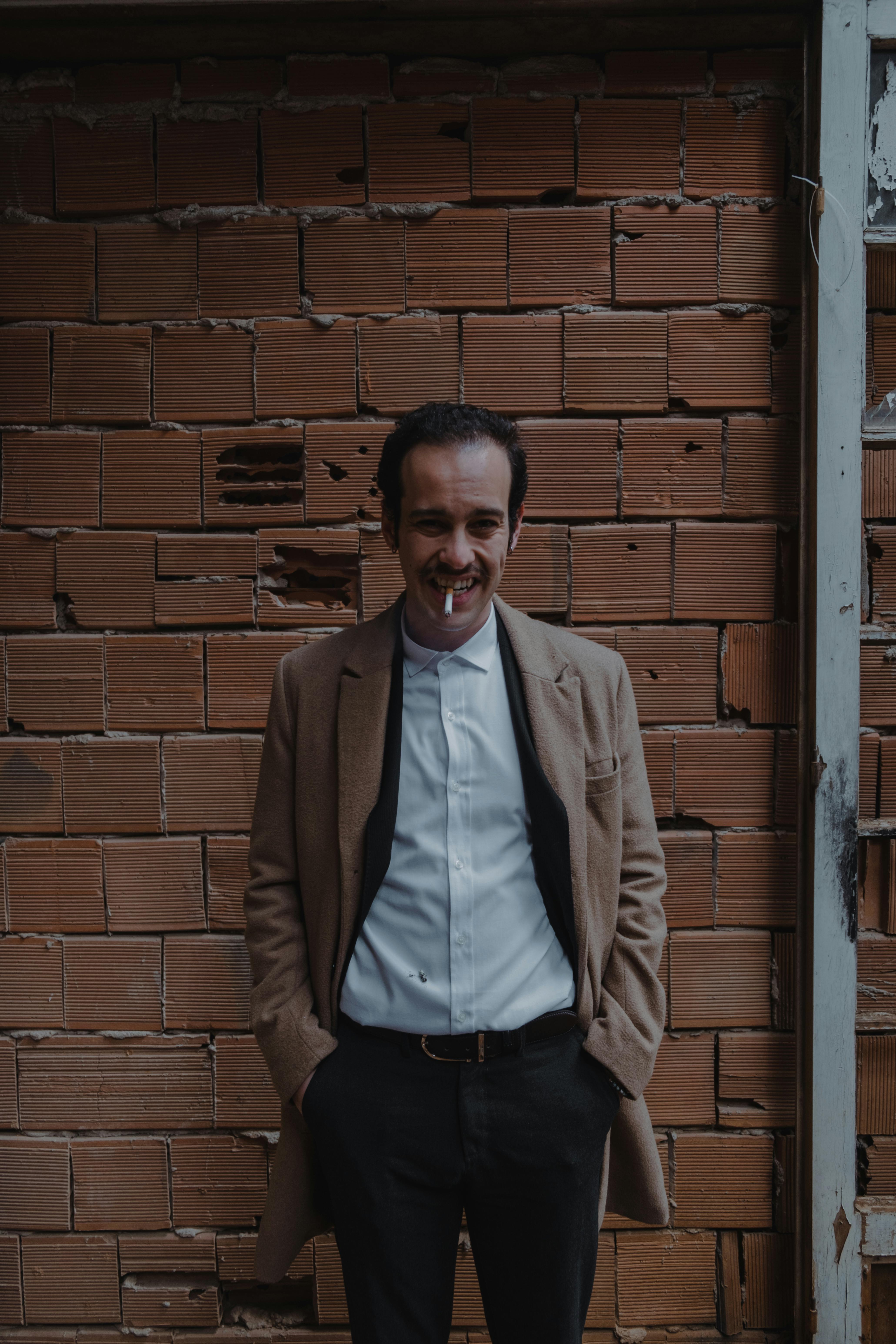 Portrait of a stylish man in menswear smoking outdoors and smiling.