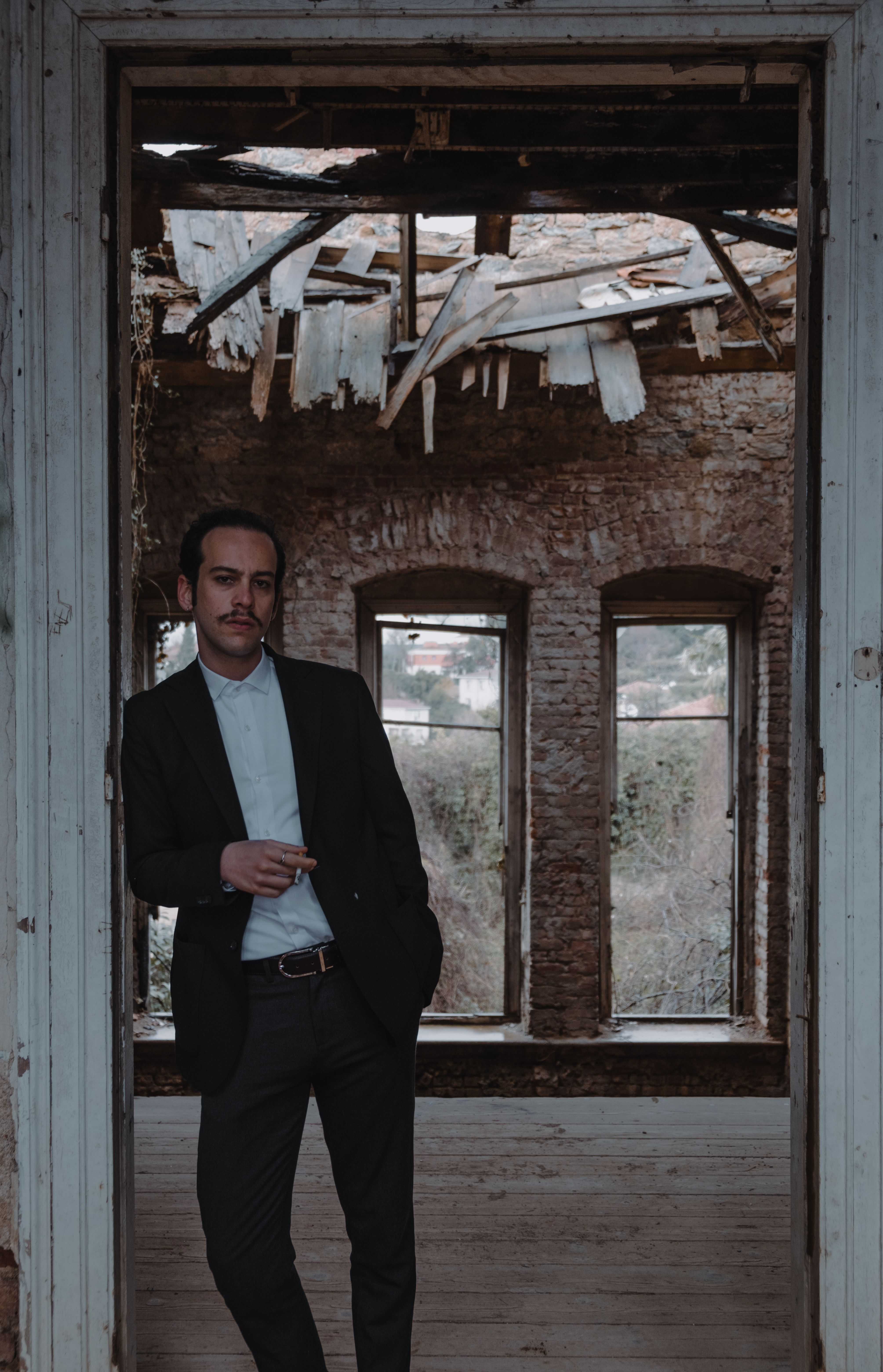 Man in a full suit standing and smoking in a deteriorated building doorway, evoking a moody atmosphere.