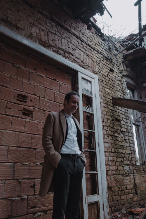 Free A man in a coat stands inside an old, ruined building with exposed brick walls. Stock Photo