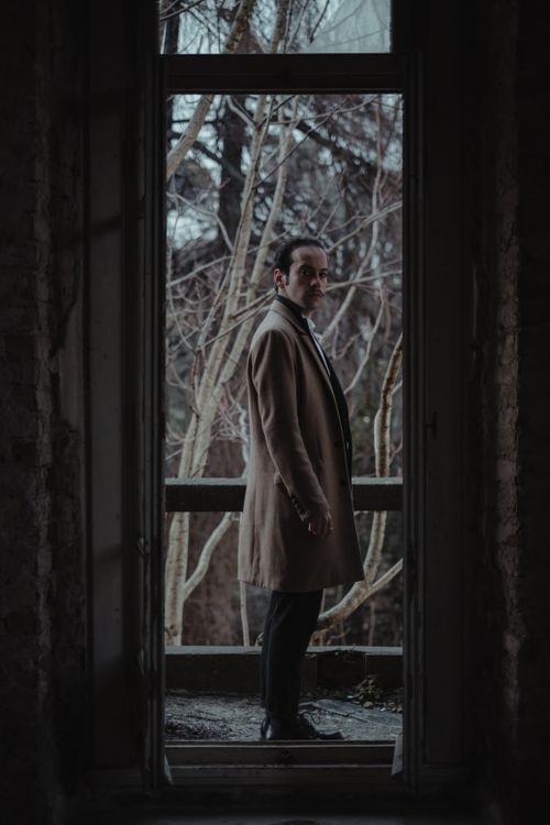 Free Stylish man in a trench coat standing on an abandoned balcony, showcasing elegance and mystery. Stock Photo