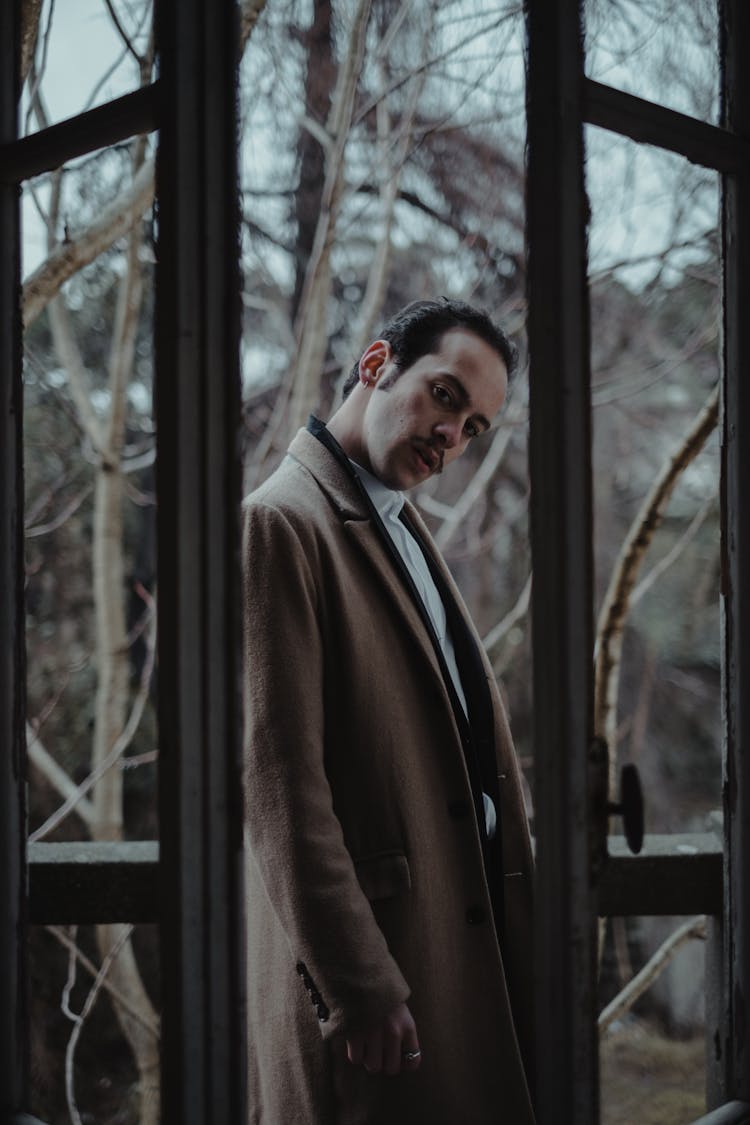 Man In Brown Coat Standing Near A Glass Door