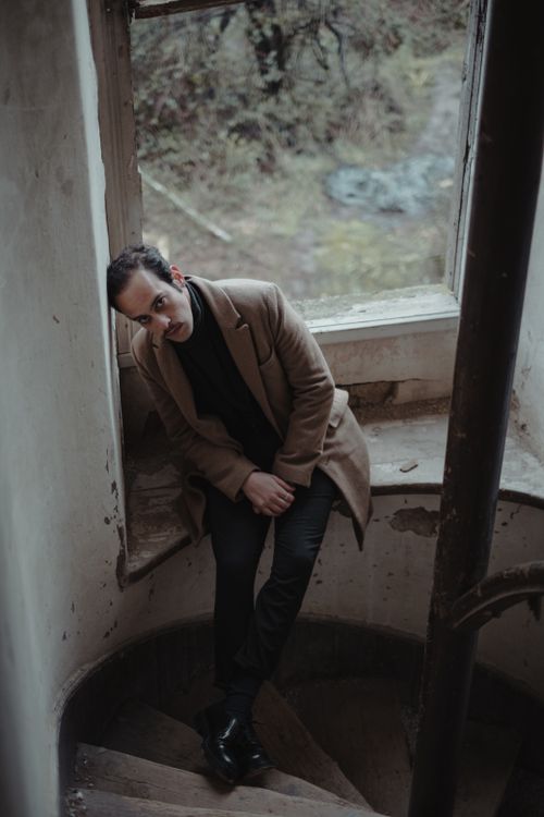 Free Stylized portrait of a man resting on a spiral staircase near a window, conveying a moody atmosphere. Stock Photo