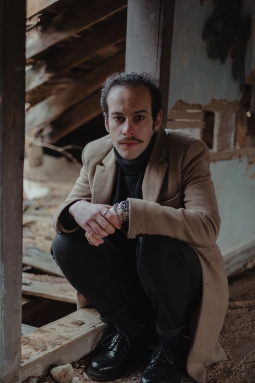 Free A man with a mustache crouches in an abandoned building, wearing a brown coat. Stock Photo