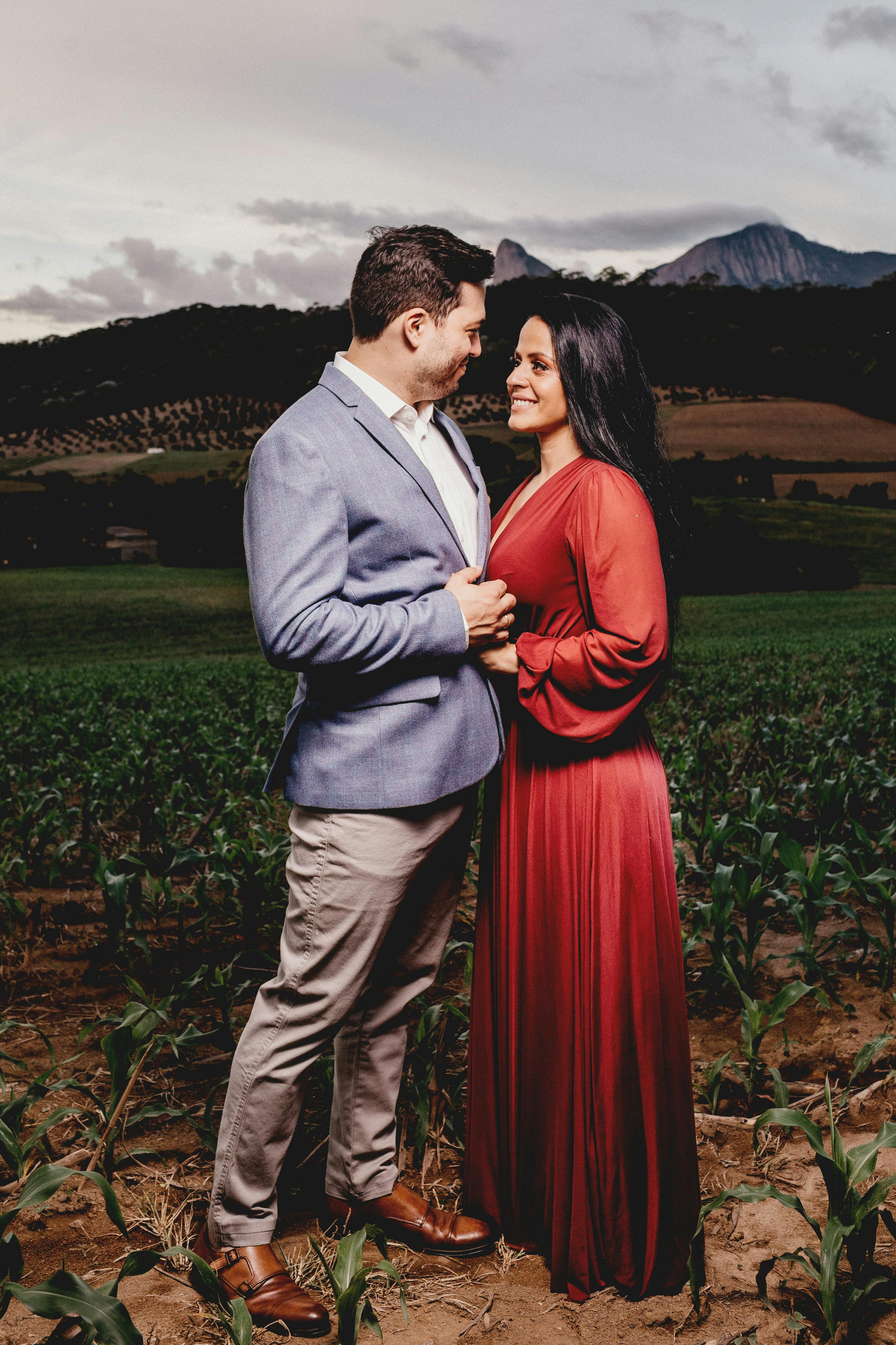 Side view of smiling Indian groom in suit holding hand of bride in dress while looking at each other in countryside