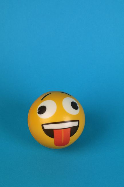 Close-up of a yellow emoji stress ball with tongue sticking out, set against a blue background.