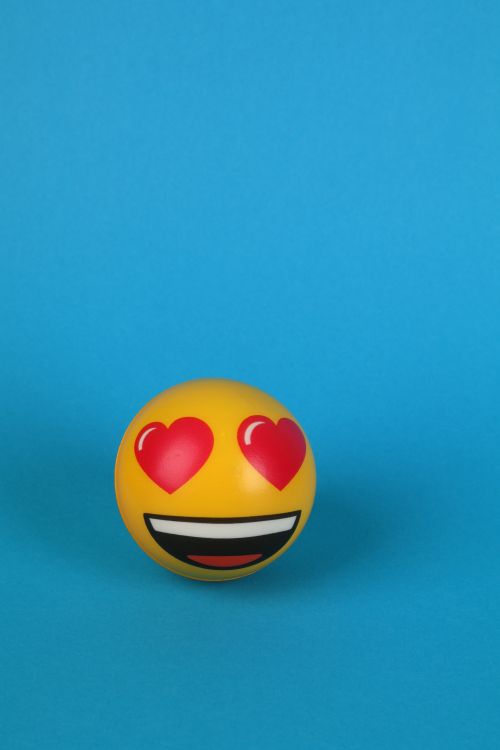 Free Bright yellow ball with heart eyes and a smile on a vibrant blue backdrop. Stock Photo