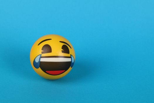 Vibrant yellow emoji ball with a laughing expression against a blue background.