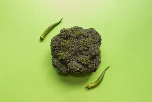 Vibrant overhead shot of fresh broccoli and okra on a green backdrop, highlighting healthy eating.