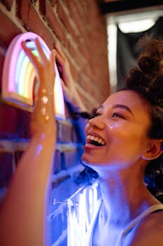 Smiling woman admiring neon rainbow lights on a brick wall.