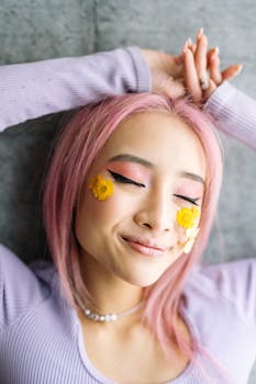 Close-up portrait of a young woman with pink hair and artistic floral makeup, exuding joy.