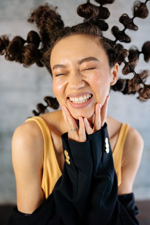 Free A young woman with a unique hairstyle and creative makeup, smiling joyfully indoors. Stock Photo