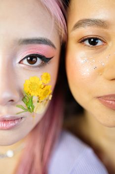 Close-up of two young women with artistic makeup featuring glitter and flowers.