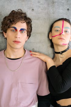Close-up portrait of a young couple with vibrant makeup against a textured background.