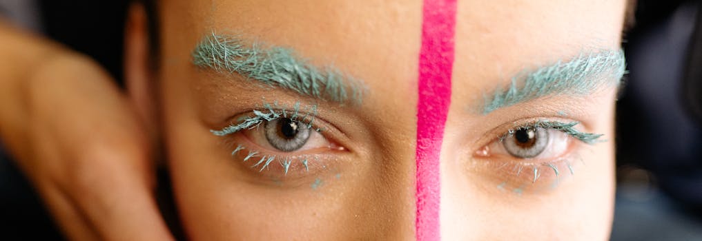 Close-up of vibrant makeup with blue eyebrows and pink line highlighting creativity and style.