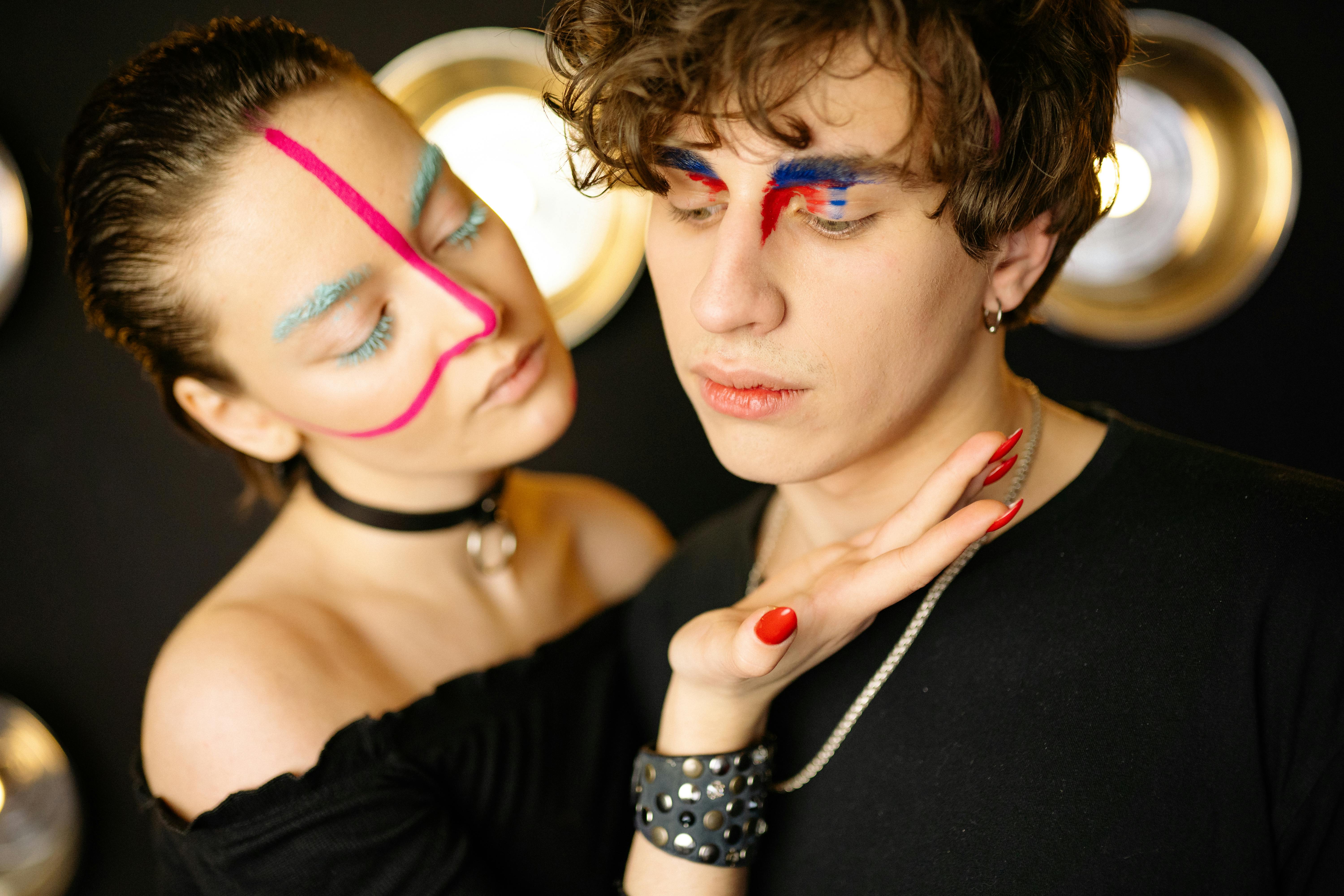 Close-up portrait of two models with striking face paint and vibrant fashion poses.