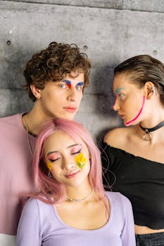 Vibrant portrait of three young adults with creative makeup expressions against a concrete wall.
