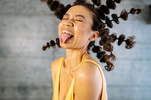 Free Energetic woman with curly hair and yellow tank top playfully sticking out tongue. Stock Photo