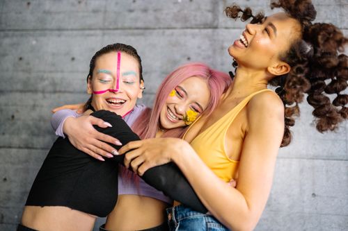 Free Three women with vibrant makeup and hairstyles laughing and hugging in a heartwarming moment. Stock Photo