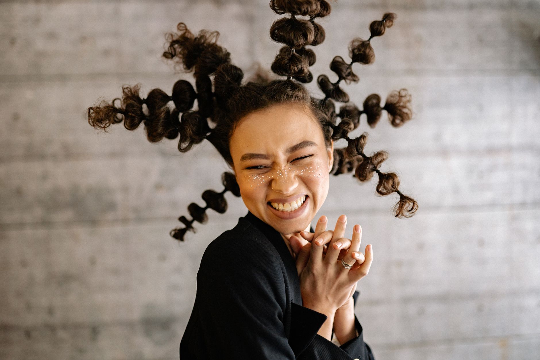 A woman with a unique hairstyle and glitter on face expressing happiness indoors.